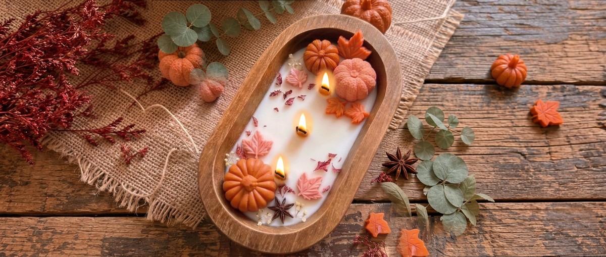 Lit pumpkin dough bowl candle with wax pumpkins, maple leaves, star anise and eucalyptus on a rustic wooden table